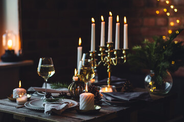 Elegant decor for Christmas family dinner. Center piece with burning candles, vintage chandelier. Zero waste eco-friendly reusable home decoration, fir tree branches. Cozy atmosphere, wooden furniture