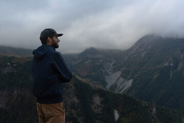 Young hiker standing on a cliff edge, enjoying the stunning panorama of the Caucasus Mountains,...
