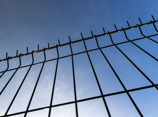 a thin metal lattice fence against a blue sky background, a small thin fence dividing the territory...
