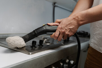 Cleaning company worker using steam cleaner with cloth attachment sanitizing grimy gas stove...