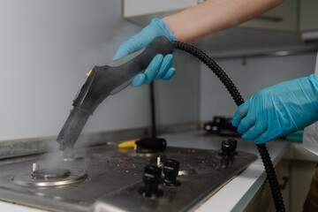 Male in gloves steam cleaning gas stove surface, eliminating burned food and grease, restoring...
