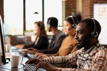 Closeup of african american call center agent reviewing information on his desktop pc while...