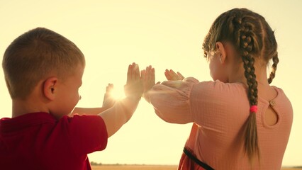 Group of happy children raise their hands to sun. Boy girl party vacation holiday in park against sun. Children prayer they stretch their hands up to sun. Sunlight in hands of child, nature. Religion