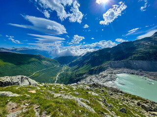 LENS FLARE: Panoramic view of a lake with melted glacial water flowing into a valley, forming the...