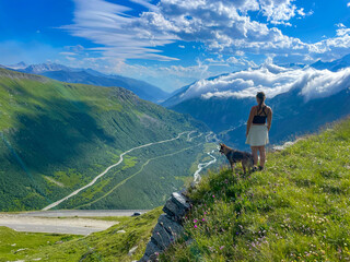Scenic viewpoint where woman and her shepherd dog admire alpine valley with a winding road and...