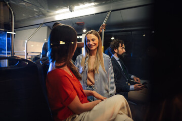 Young women talking on a bus at night with businessman using a smartphone