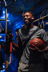 Smiling basketball player holding ball and water bottle on bus at night