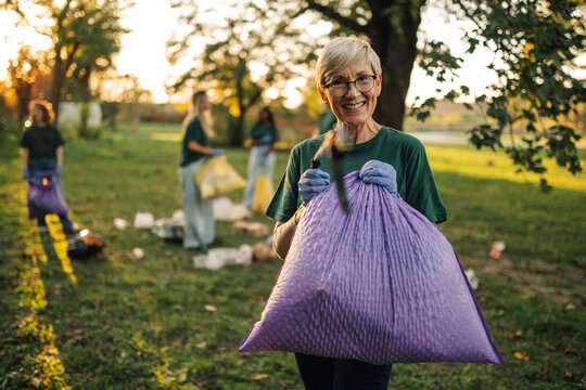 Senior woman volunteer holding trash bag cleaning park