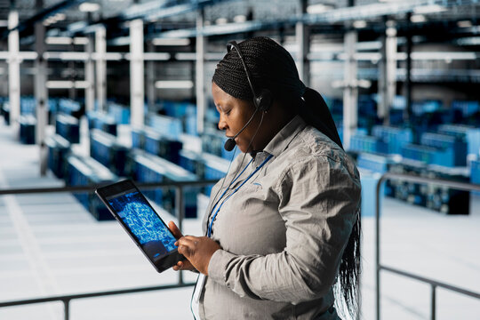 Data center engineer dispatching field technicians after doing AI system scans using tablet. Female technical support specialist in server room managing live support calls during server errors
