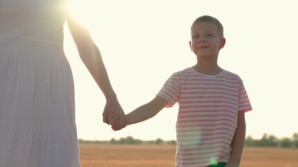 Child mom walking in summer park in sun, family happiness concept. Child, son, mom holding hands, mothers kid. Happy family relaxing in nature. Loving Parent, child boy, walking together on sunny day