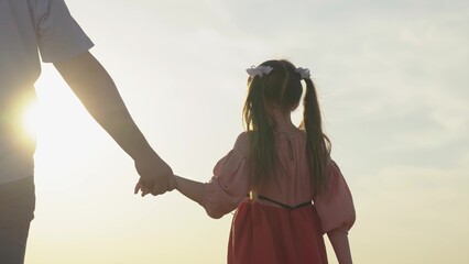 Dad takes hand of child in sun, happy family outdoor. Family holiday. Parent, daughter, child carefree childhood. Father, girl stand together, hold hands closeup, teamwork. Paternity, baby love, trust