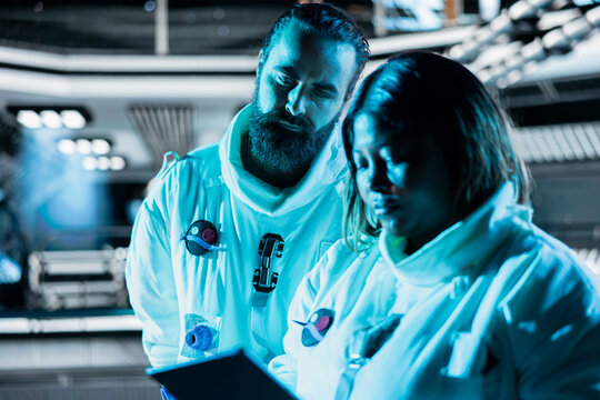 Teamworking cosmonauts exploring planetary surfaces, preparing for mission outside. Orbital station coworkers beginning landing procedures on blue planet, mapping unknown worlds