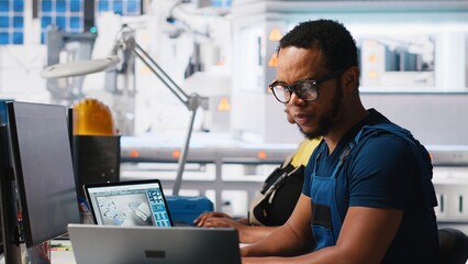 Black engineer inputs solar system parameters at industrial workstation, using PC in a renewable...