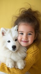 Portrait of a smiling child girl in yellow sweater hugging fluffy white spitz dog on solid pastel yellow background