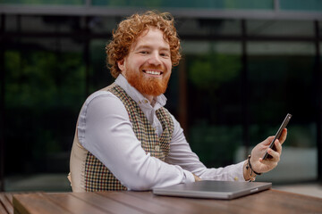 A cheerful professional sits at a table, working with a laptop and smartphone in a contemporary...