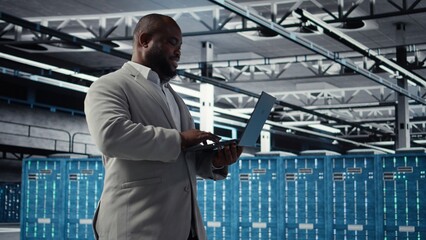 Fototapeta premium Server farm IT specialist using laptop to improve deep learning AI systems workloads. Data center software developer using notebook to adjust artificial intelligence model parameters, camera A