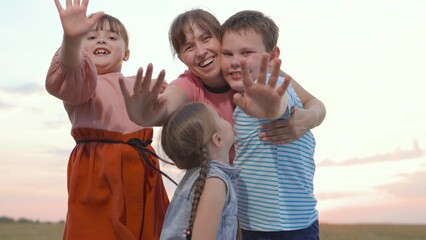 Mother, children play in park. Happy family concept. Mom, Children happily wave their hands, look at camera. Happy child laughing in park. Faces of child, children emotion of happiness at sunset sky