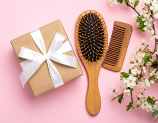 Rustic wooden hairbrush and comb placed beside beautifully wrapped gift on soft pink backdrop, complemented by delicate flowers, creating serene and inviting atmosphere