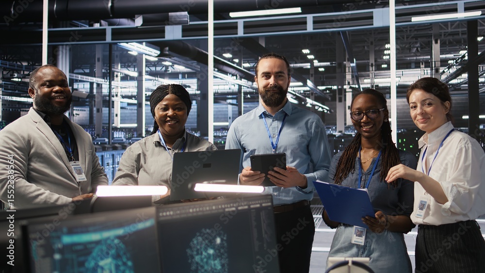 Poster smiling engineering team in server room reviewing infrastructure diagnostics on devices. it professi