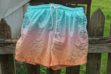 one colored swimming shorts hanging on gray wooden fence on summer street