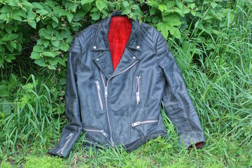 one black leather jacket with red fur lies on  vegetation and green grass on a summer street