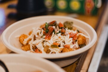 Bowl of loaded tater tots topped with shredded cheese, pico de gallo and jalapeños in a compostable bowl on a wooden table