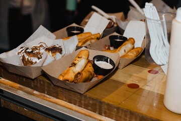 Paper trays of crispy fried taquitos with dipping sauces and dessert in the background on a wooden prep counter