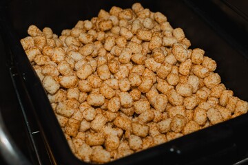 Bulk container of crispy tater tots piled in a foodservice bin at a restaurant kitchen prep station
