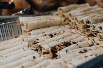 Bulk rolled tortillas (flautas/taquitos) arranged in a metal catering tray ready for cooking in a...