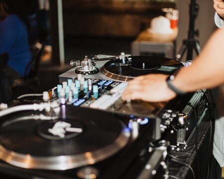 Close-up of DJ mixer and dual turntables with vinyl records and hands adjusting controls at a live event