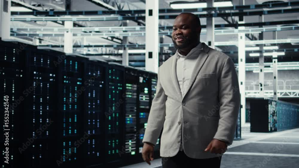 Poster smiling engineer walking in data center workplace with multiple rows of fully operational supercompu