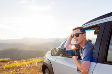 Young traveler leans out the car window, enjoying the view and the freedom of a road trip. A...