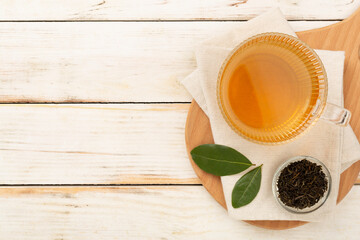 Cup of tea with dry and fresh leaves on wooden background, top view