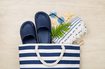 Blue beach bag with summer accessories on wooden background, top view