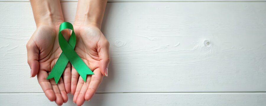 Hands hold green ribbon on white wood background. Mental health concept, symbol of awareness. Support, hope, care, world mental health day, medical awareness, october campaign.