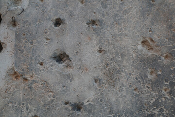 An abstract close-up photograph of a grey surface heavily scarred with bullet and shrapnel holes...