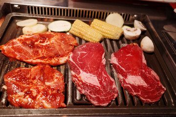 Raw ingredients are laid out on a tabletop grill, ready for a Korean BBQ or Japanese Yakiniku meal.