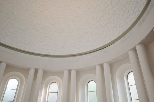 An upward view of the stunning architectural interior of a modern rotunda. The focus is on the expansive domed ceiling, which features an intricate geometric relief pattern.