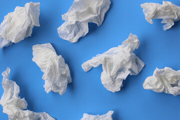 Used crumpled tissues scattered on a blue surface.