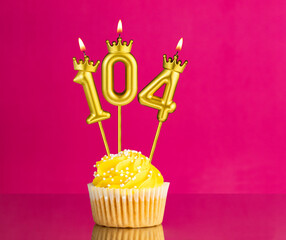 Yellow birthday cupcake with a number 104 candle - Birthday card on a pink background