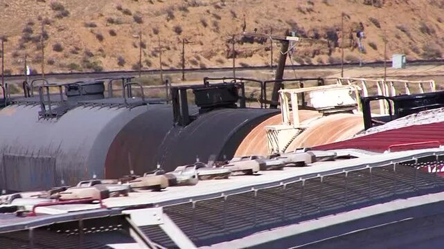 Telephoto-compressed shot of a railroad train of grain hopper and tank cars going around a bend, emphasizing roof detail, in an arid landscape near Bakersfield, California.