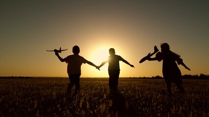 Children play with toy plane. Happy children run with toy plane across field at sunset. Boy, girl wants to become pilot, astronaut. Teenager dreams of flying, becoming pilot. Silhouette