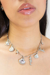 An unrecognizable woman models a silver necklace around her neck against a white background in...