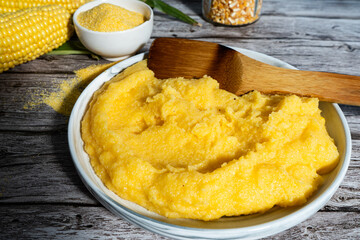 Creamy polenta being served with corn on the cob and cornmeal on rustic wooden table