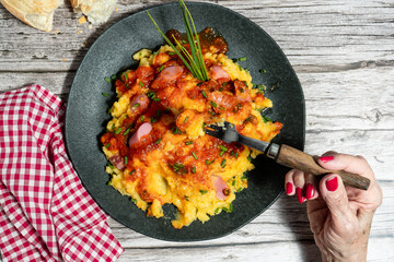 Woman eating polenta with sausage, tomato sauce and chives on rustic wooden table