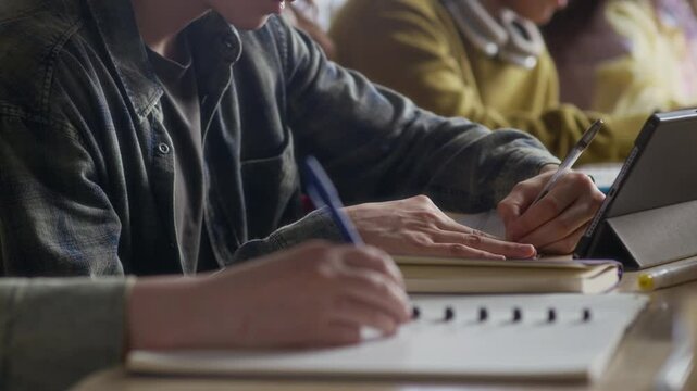 Handheld shot of multiethnic group of zoomers taking notes and communicating during lecture in tiered auditorium