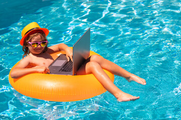 Summer business. Kid remote working on laptop in pool. Little business man working online on laptop...