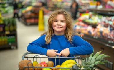 Child shopping in grocery store. Kid in supermarket. Child with shopping cart full of fruit. Kid...
