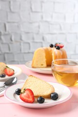 Tasty bundt cake with berries and tea on pink wooden table, closeup