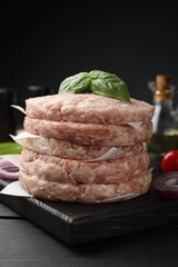 Fresh raw patties for burger and spices on black wooden table, closeup